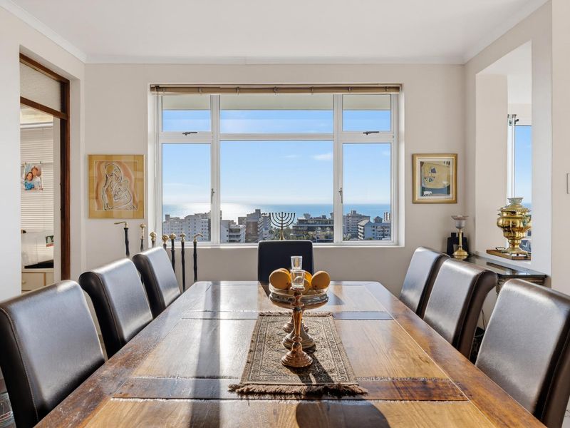 A well-lit dining room featuring a large window with expansive coastal and city views, providing a bright and airy atmosphere.