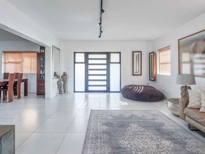 Spacious open-plan living and dining area featuring modern tiled flooring, track lighting, and a contemporary glass-paneled front entrance.