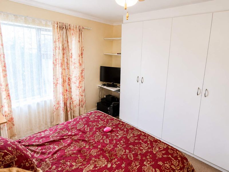 A bedroom featuring a large white built-in wardrobe, built-in shelving, and a ceiling fan, offering functional storage space.
