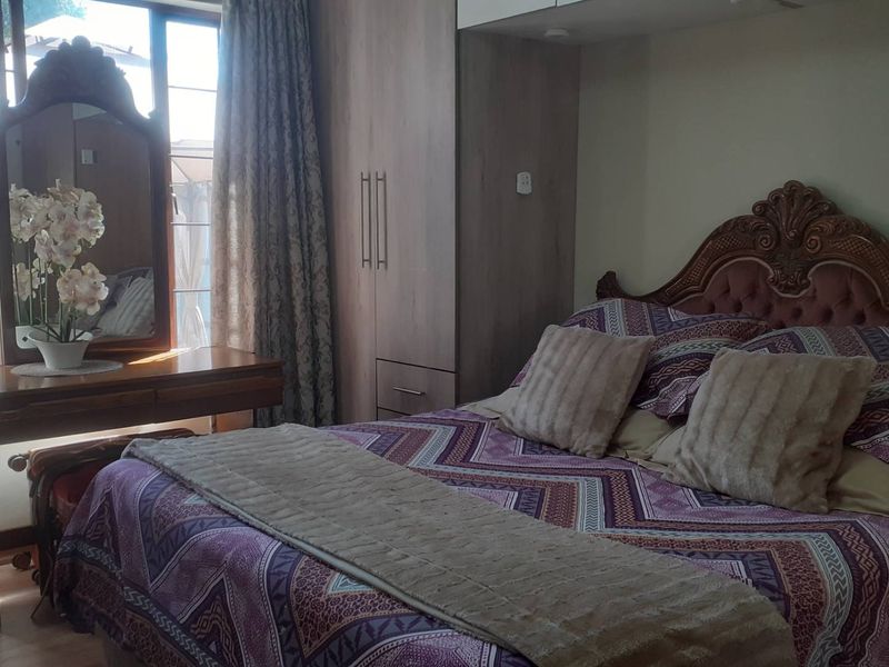 A bedroom featuring built-in cupboards, laminate flooring, and natural light from a large window.