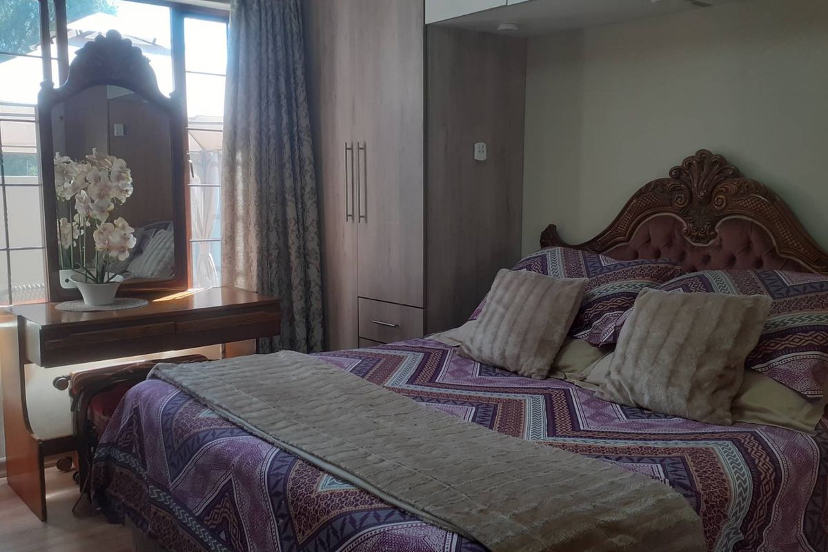 A bedroom featuring built-in cupboards, laminate flooring, and natural light from a large window.