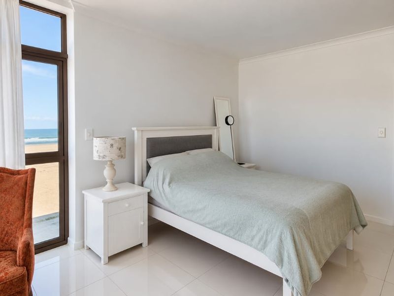 A bright bedroom featuring tiled flooring and a large glass sliding door offering direct views of the beach.
