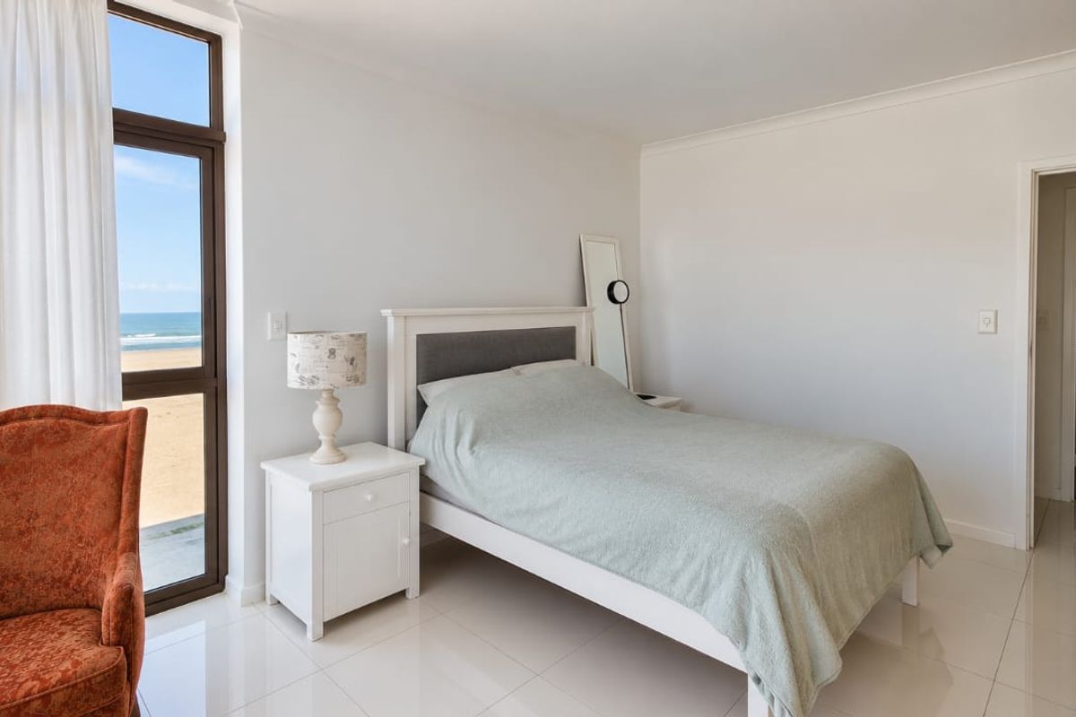 A bright bedroom featuring tiled flooring and a large glass sliding door offering direct views of the beach.