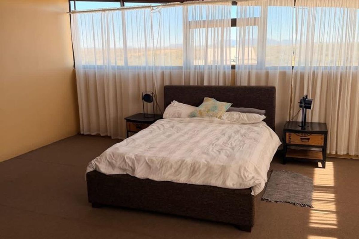 Spacious bedroom featuring large windows with natural light, exposed structural ceiling beams, and neutral carpeting.
