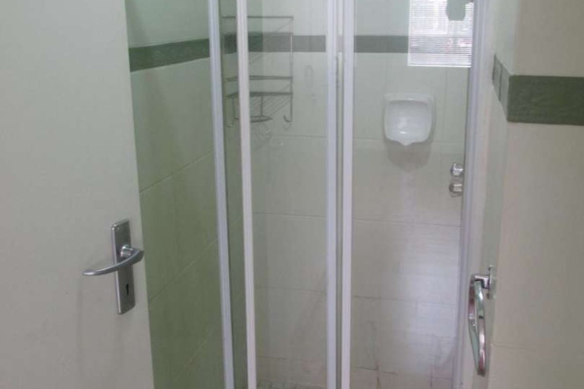A functional bathroom featuring a tiled shower enclosure with a sliding glass door and wall-mounted shower head.