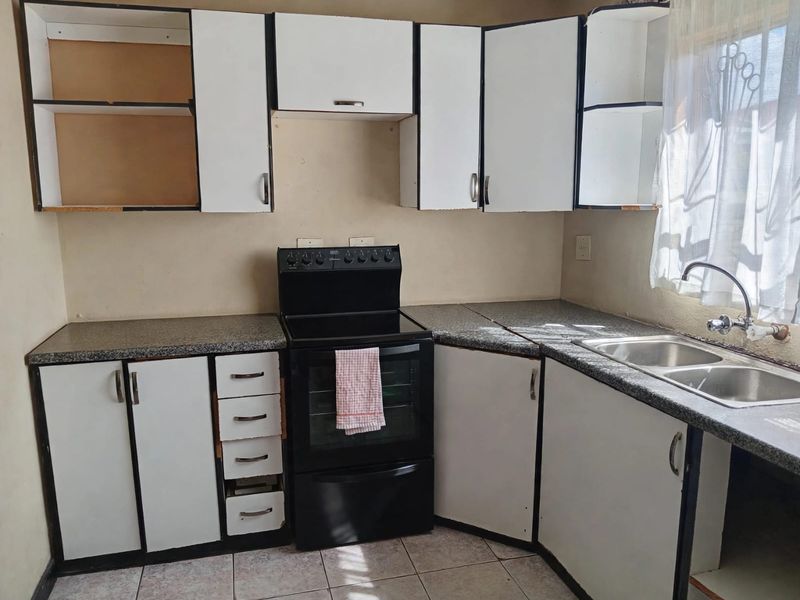 A functional kitchen featuring white cabinetry, laminate countertops, a double bowl sink, and a freestanding stove, requiring cosmetic updates to improve its overall condition.