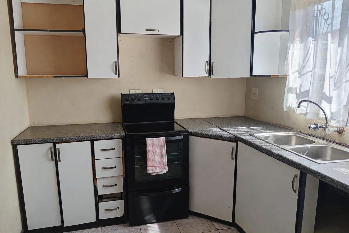A functional kitchen featuring white cabinetry, laminate countertops, a double bowl sink, and a freestanding stove, requiring cosmetic updates to improve its overall condition.