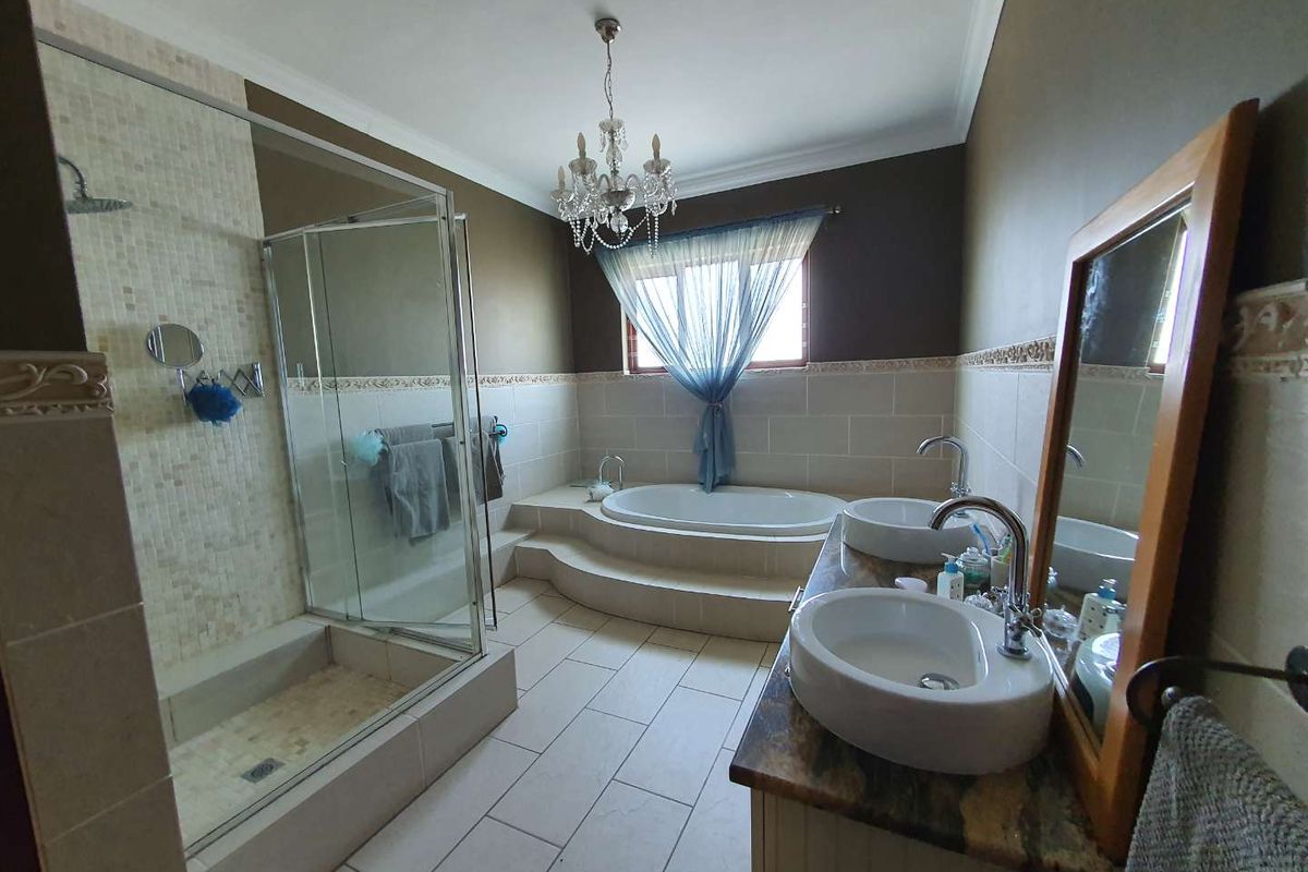 Spacious bathroom featuring a raised built-in bathtub, a glass-enclosed shower with mosaic tiling, and a double vanity with stone countertops.