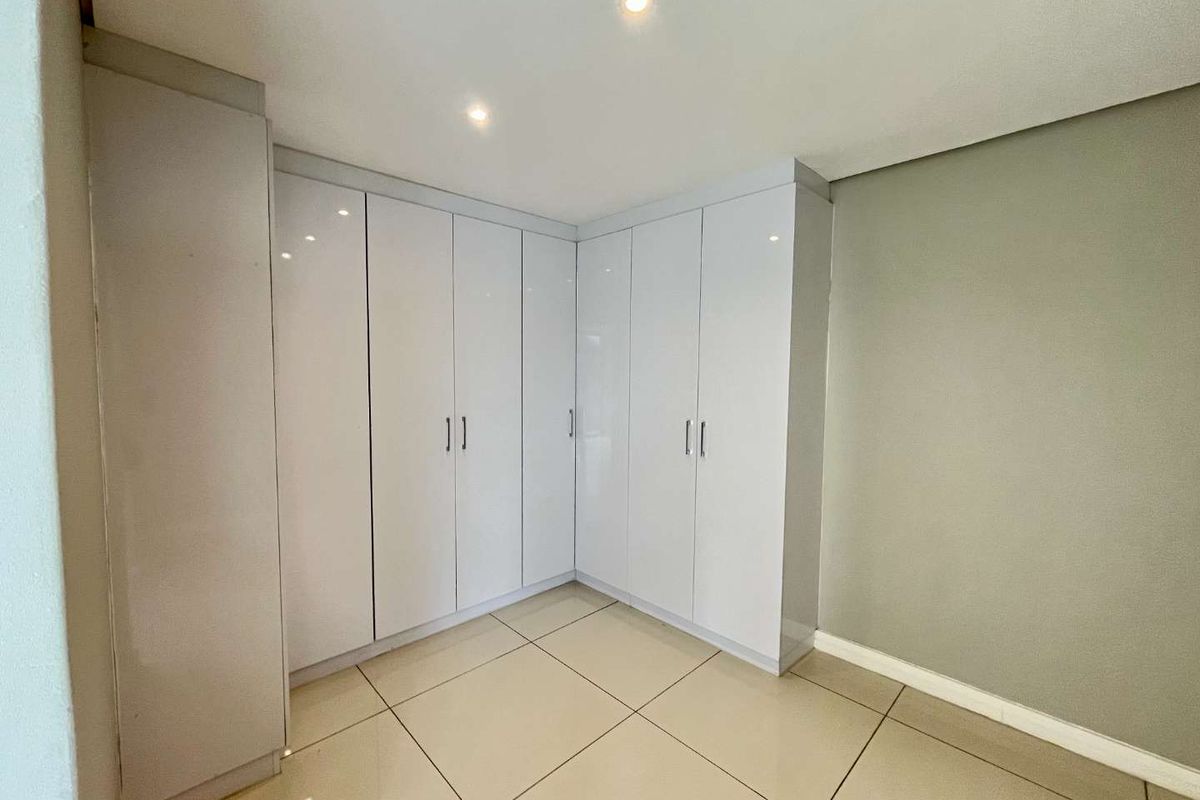 A bedroom featuring modern, floor-to-ceiling white built-in cupboards and neutral tiled flooring, offering clean lines and ample storage space.