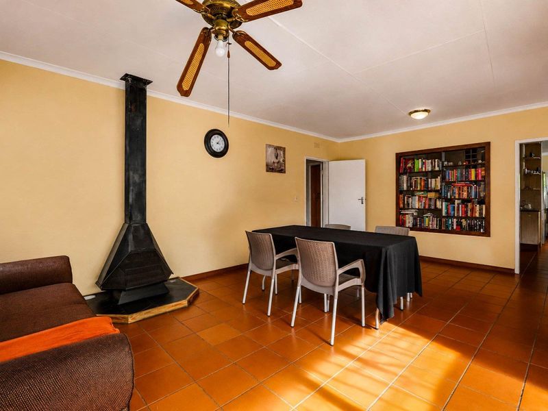 Living room featuring a freestanding fireplace, built-in bookshelf, ceiling fan, and terracotta-style tiled flooring.