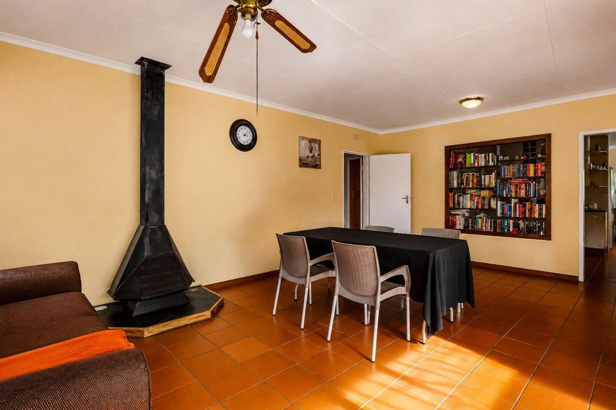 Living room featuring a freestanding fireplace, built-in bookshelf, ceiling fan, and terracotta-style tiled flooring.