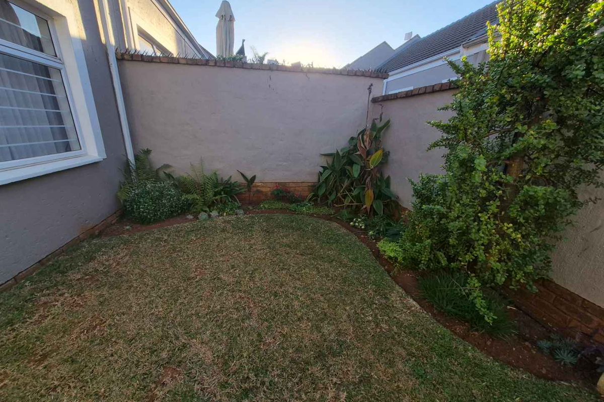 A private rear garden area featuring a small lawn, established perimeter landscaping, and high boundary walls for added privacy.