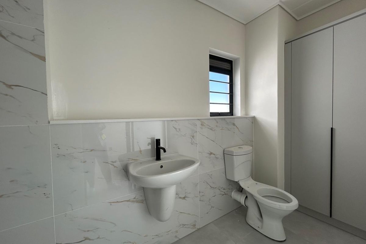 Modern bathroom featuring marble-look wall tiling, a wall-mounted basin with a black faucet, a white toilet, and built-in cabinetry.