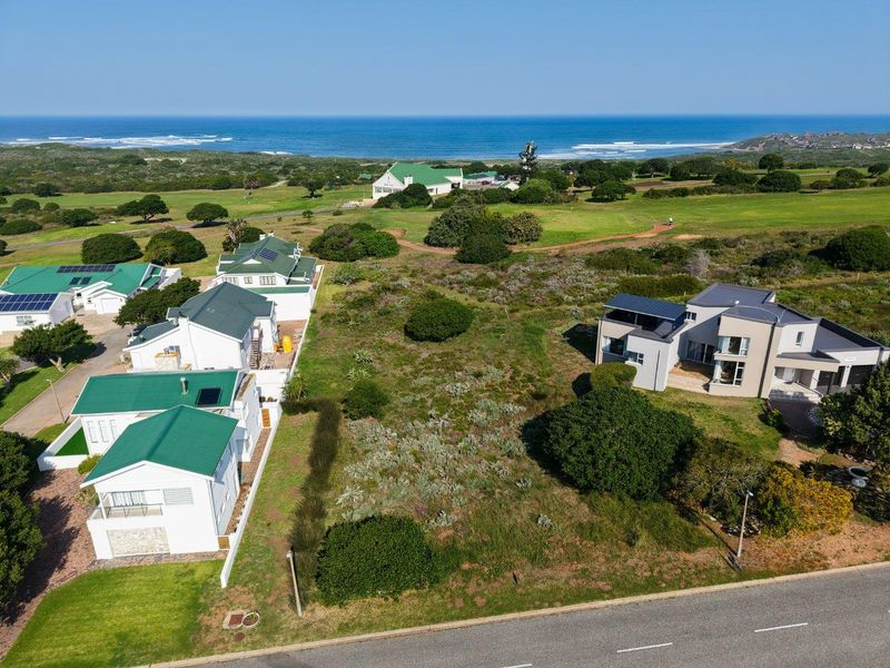 An aerial view of a vacant residential plot situated in a coastal estate, offering proximity to existing homes and scenic ocean views.