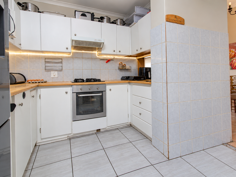 A functional kitchen featuring white cabinetry, wooden countertops, a tiled backsplash with under-cabinet lighting, and integrated cooking appliances.