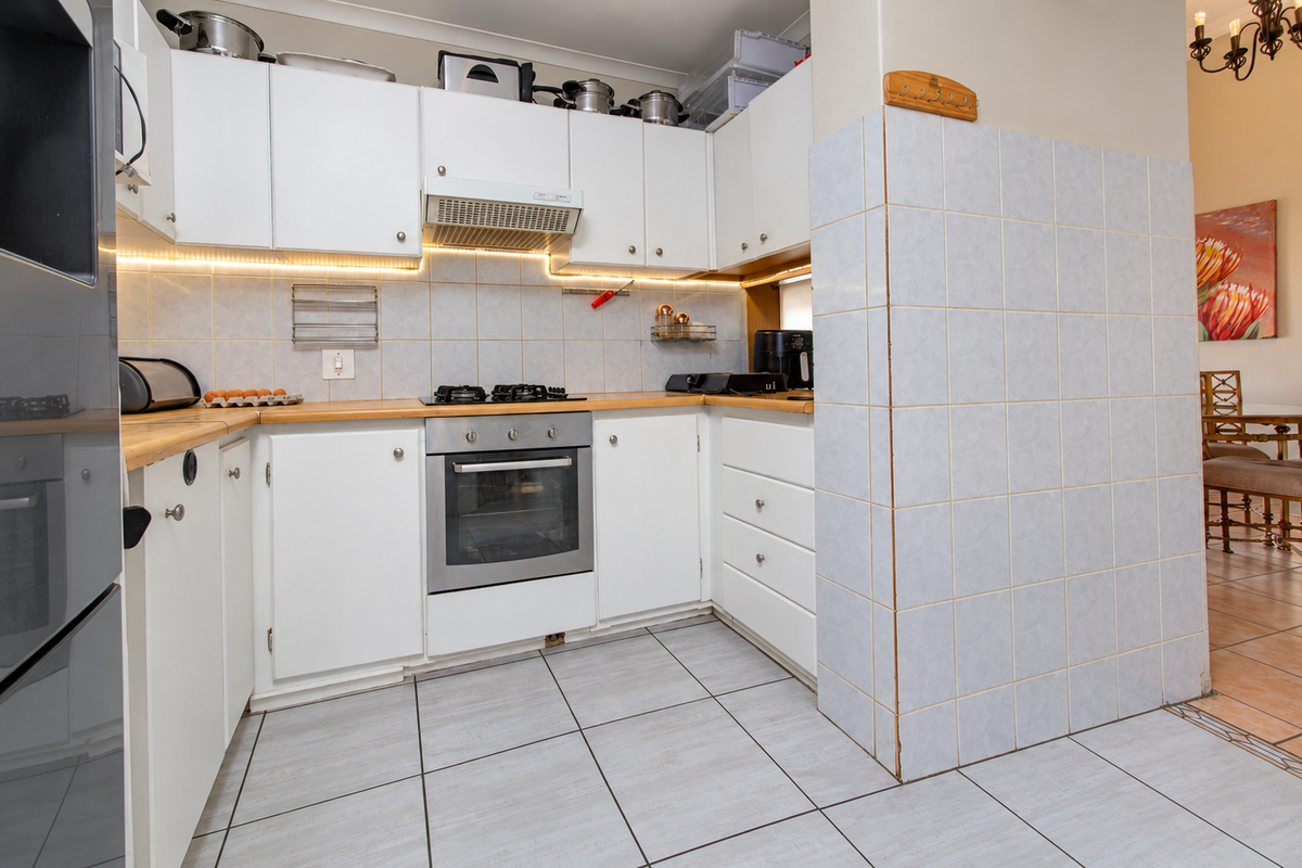A functional kitchen featuring white cabinetry, wooden countertops, a tiled backsplash with under-cabinet lighting, and integrated cooking appliances.