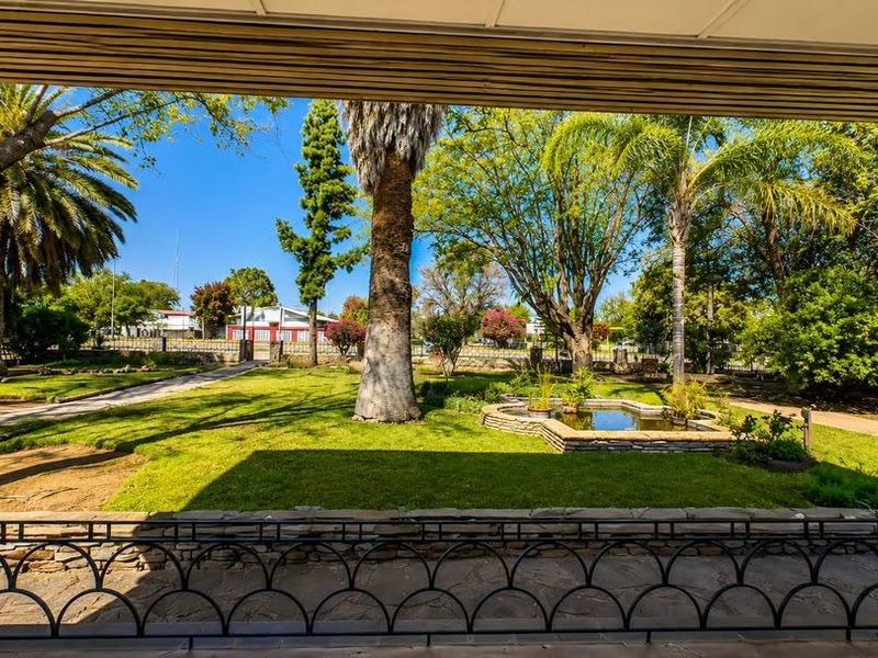 A covered patio overlooking a well-maintained garden featuring a stone-edged water feature, mature trees, and stone-clad architectural pillars.