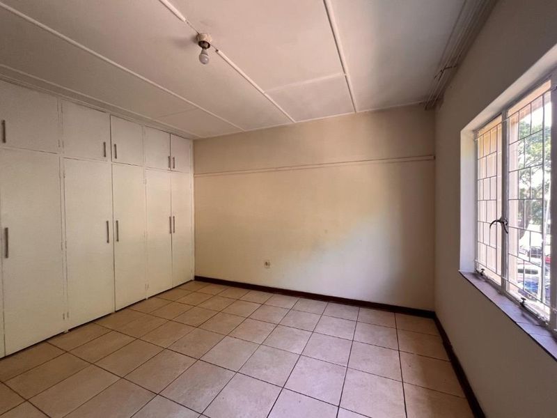 An empty bedroom featuring built-in cupboards, tiled flooring, and security bars on the window, offering a blank canvas for renovation.