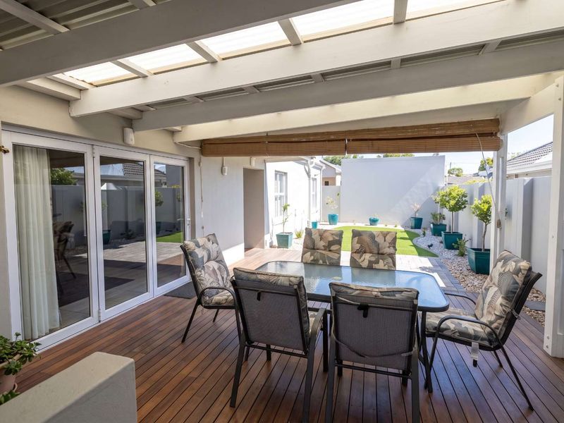 A covered outdoor patio featuring timber decking, a pergola with translucent roofing, and bifold doors leading into the home, overlooking a private garden.