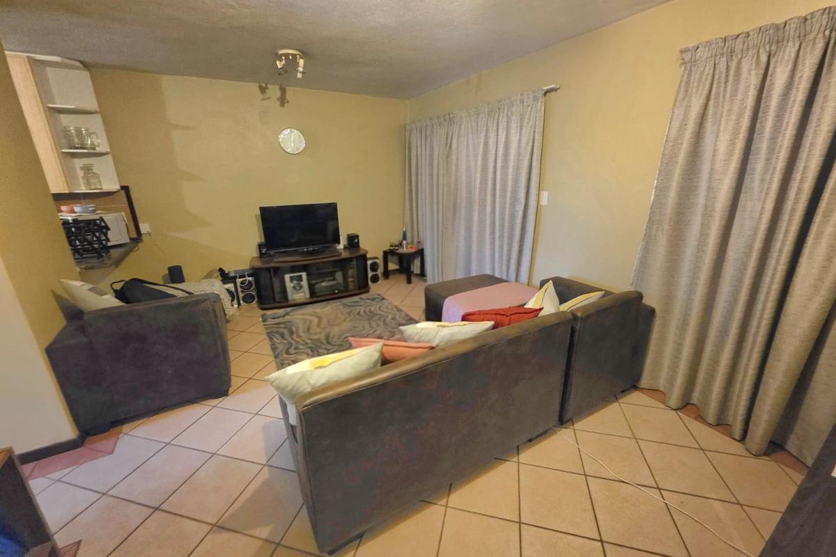 A living room area featuring ceramic floor tiles, a sliding glass door, and built-in shelving, currently showing signs of wear.