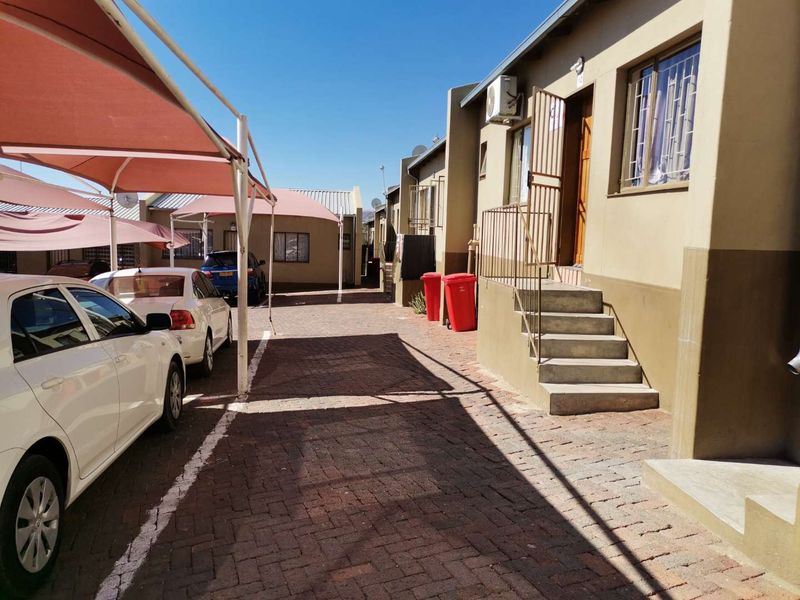 Exterior view of a townhouse complex featuring a paved driveway, covered parking bays, and direct access stairs to the unit entrance.