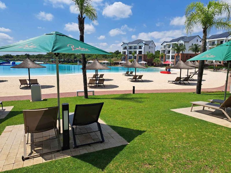A well-maintained communal pool area featuring a large swimming pool, sandy beach area, and landscaped lawns within a modern apartment complex.