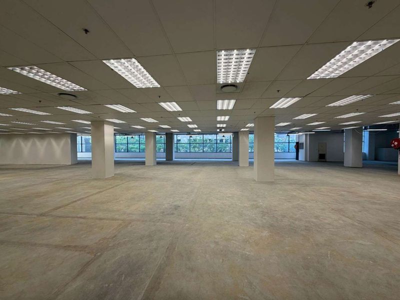 Expansive open-plan retail or office space featuring a suspended ceiling, recessed lighting, concrete flooring, and large windows providing ample natural light.