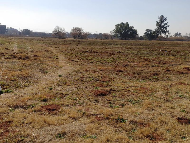 A wide-angle view of a vacant commercial land plot featuring open, undeveloped terrain with sparse vegetation.