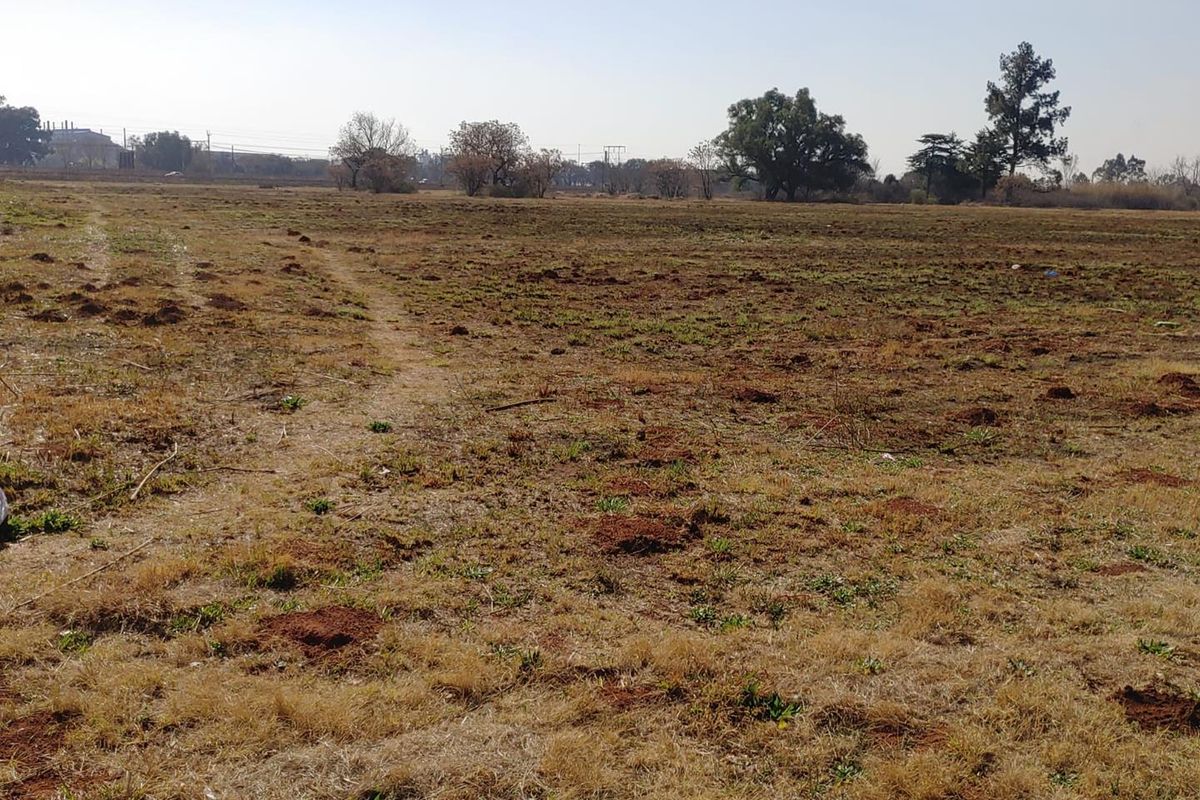 A wide-angle view of a vacant commercial land plot featuring open, undeveloped terrain with sparse vegetation.
