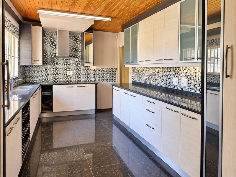 Modern kitchen featuring light wood cabinetry, dark granite countertops, mosaic tile backsplash, and a timber ceiling, offering a clean and functional workspace.