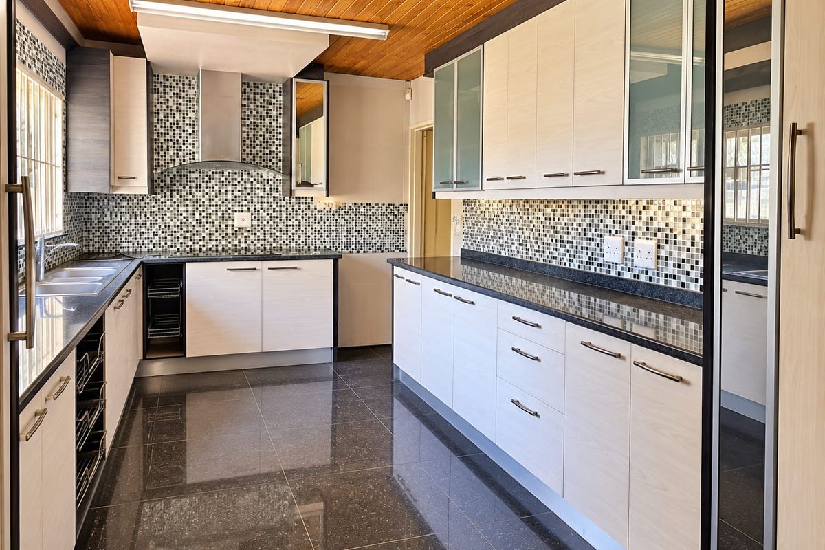 Modern kitchen featuring light wood cabinetry, dark granite countertops, mosaic tile backsplash, and a timber ceiling, offering a clean and functional workspace.