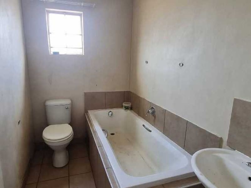 A compact bathroom featuring a built-in bathtub, toilet, and pedestal basin with tiled flooring and splashbacks, requiring cosmetic updates.
