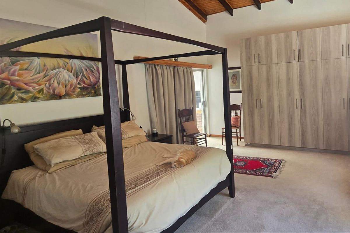 Spacious bedroom featuring high vaulted timber ceilings, neutral carpeting, and extensive built-in cabinetry with sliding door access to an outdoor area.