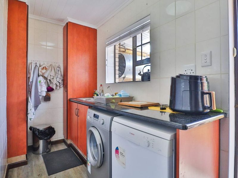 A functional laundry area featuring built-in cabinetry, a granite countertop, and a stainless steel sink with tiled splashback.