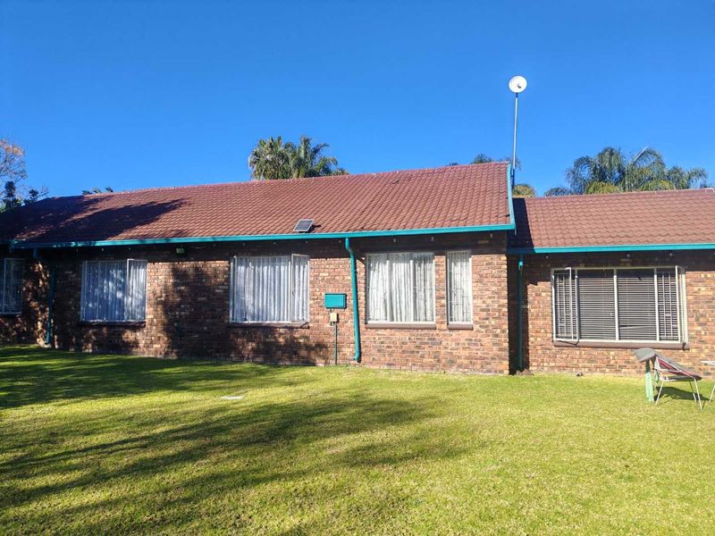 Rear view of a single-story brick house featuring a tiled roof, established lawn, and multiple windows with fitted blinds.
