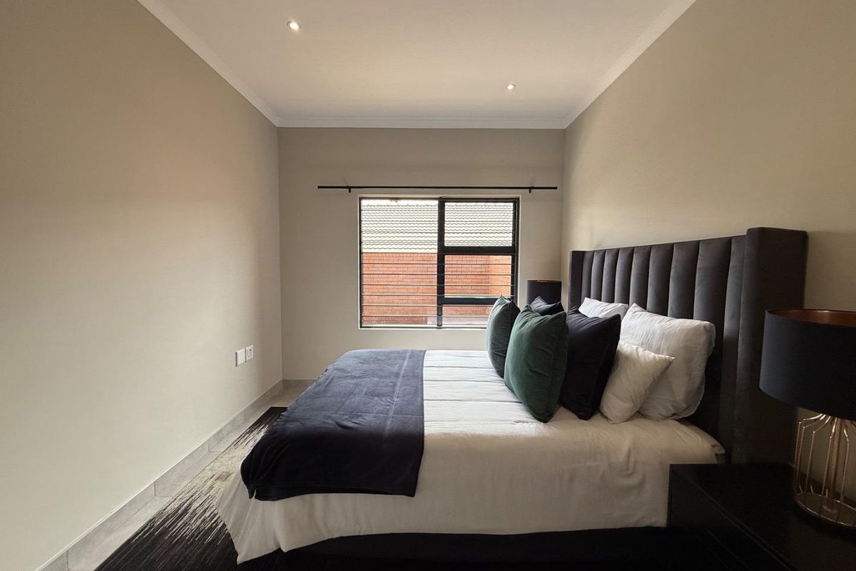 A well-maintained bedroom featuring neutral wall tones, recessed ceiling lighting, and a large window with dark framing.