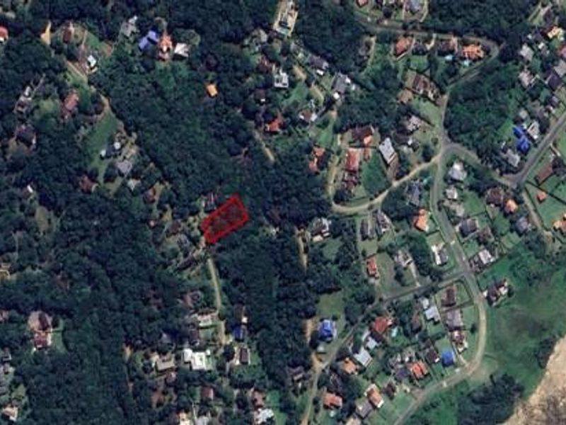 Aerial view of a residential vacant land plot highlighted in red, situated within a coastal neighborhood surrounded by dense vegetation.