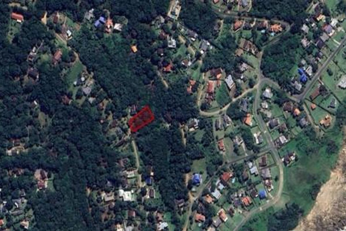 Aerial view of a residential vacant land plot highlighted in red, situated within a coastal neighborhood surrounded by dense vegetation.