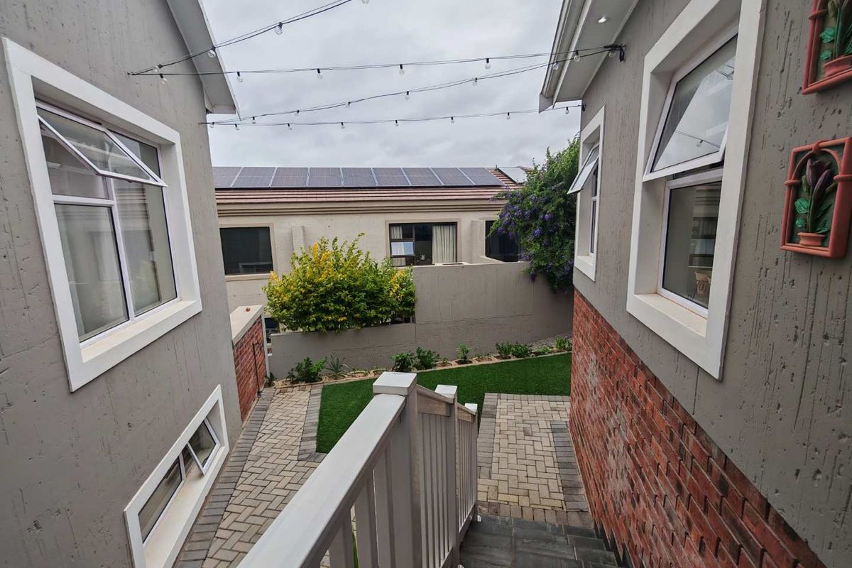 A view looking down from a staircase towards a paved courtyard area with artificial lawn, bordered by brick and rendered exterior walls.