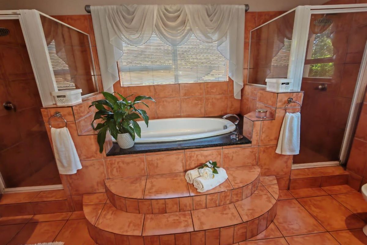 A spacious bathroom featuring a raised built-in bathtub with tiled steps, flanked by dual shower enclosures and finished with warm-toned ceramic tiling.