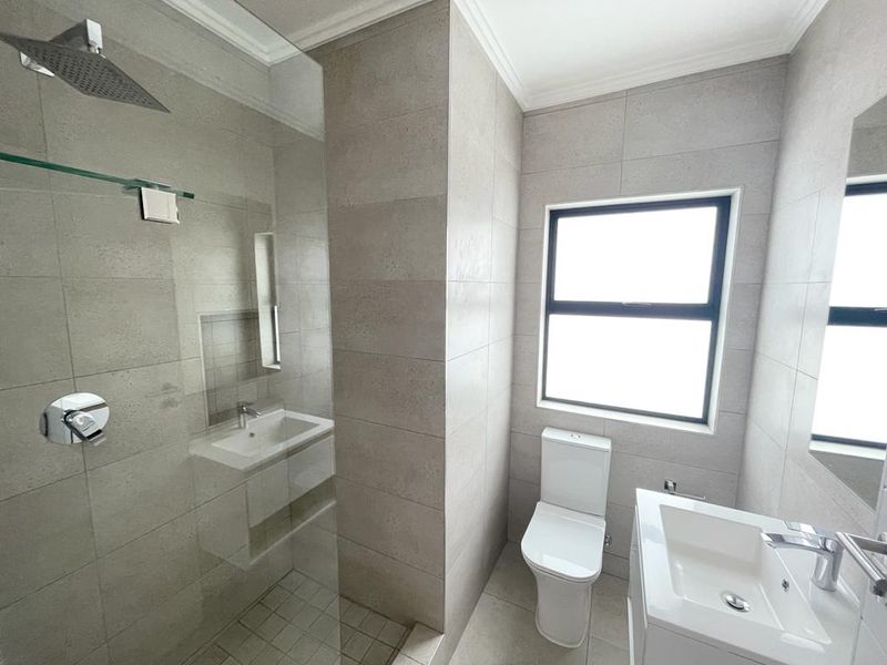 Modern bathroom featuring a walk-in shower with a rain shower head, wall-mounted toilet, and a sleek vanity basin with neutral floor-to-ceiling tiling.