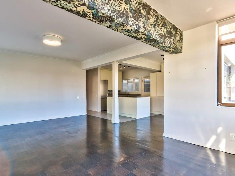 Spacious open-plan living and kitchen area featuring dark parquet flooring, a central kitchen island, and neutral cabinetry, offering a versatile layout for modern living.