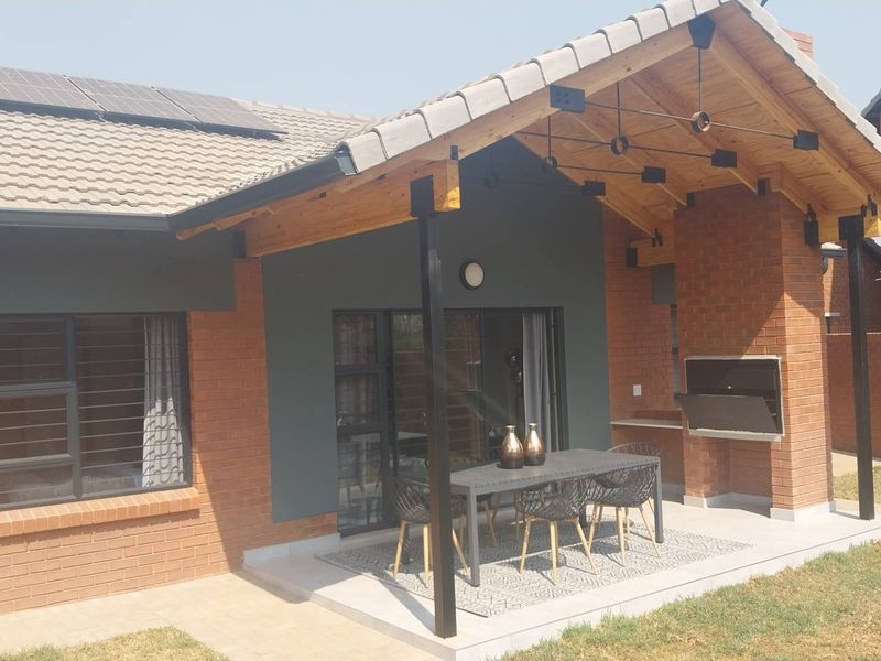 A well-maintained covered patio featuring exposed timber rafters, a built-in braai, and direct access to the interior through sliding glass doors.