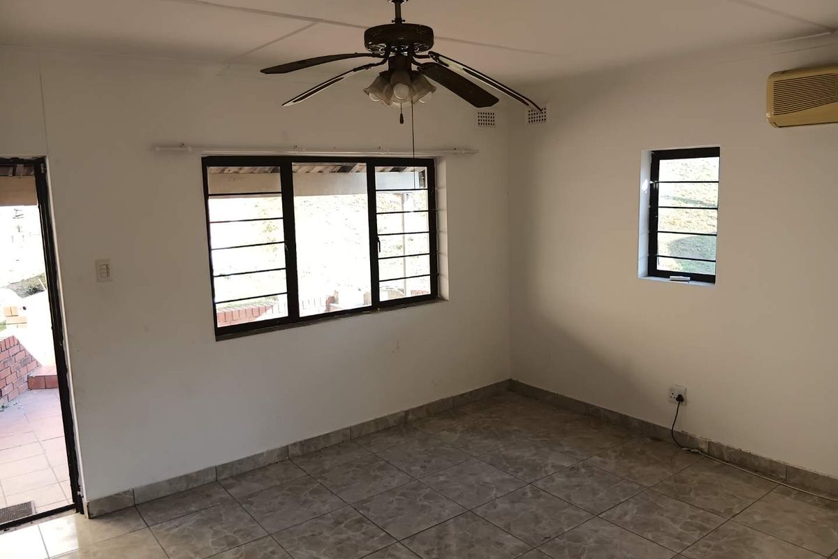 An empty living room featuring tiled flooring, a ceiling fan, and wall-mounted air conditioning, with direct access to an outdoor patio area.