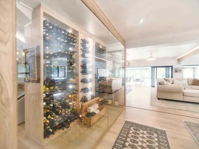 A sophisticated, custom-built glass-enclosed wine cellar featuring integrated lighting and timber cabinetry, seamlessly integrated into the open-plan living area.