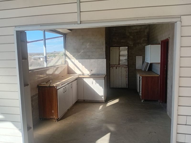 A rustic kitchen area featuring built-in cabinetry, tiled backsplash, and a stable door, requiring cosmetic updates to improve the overall finish.
