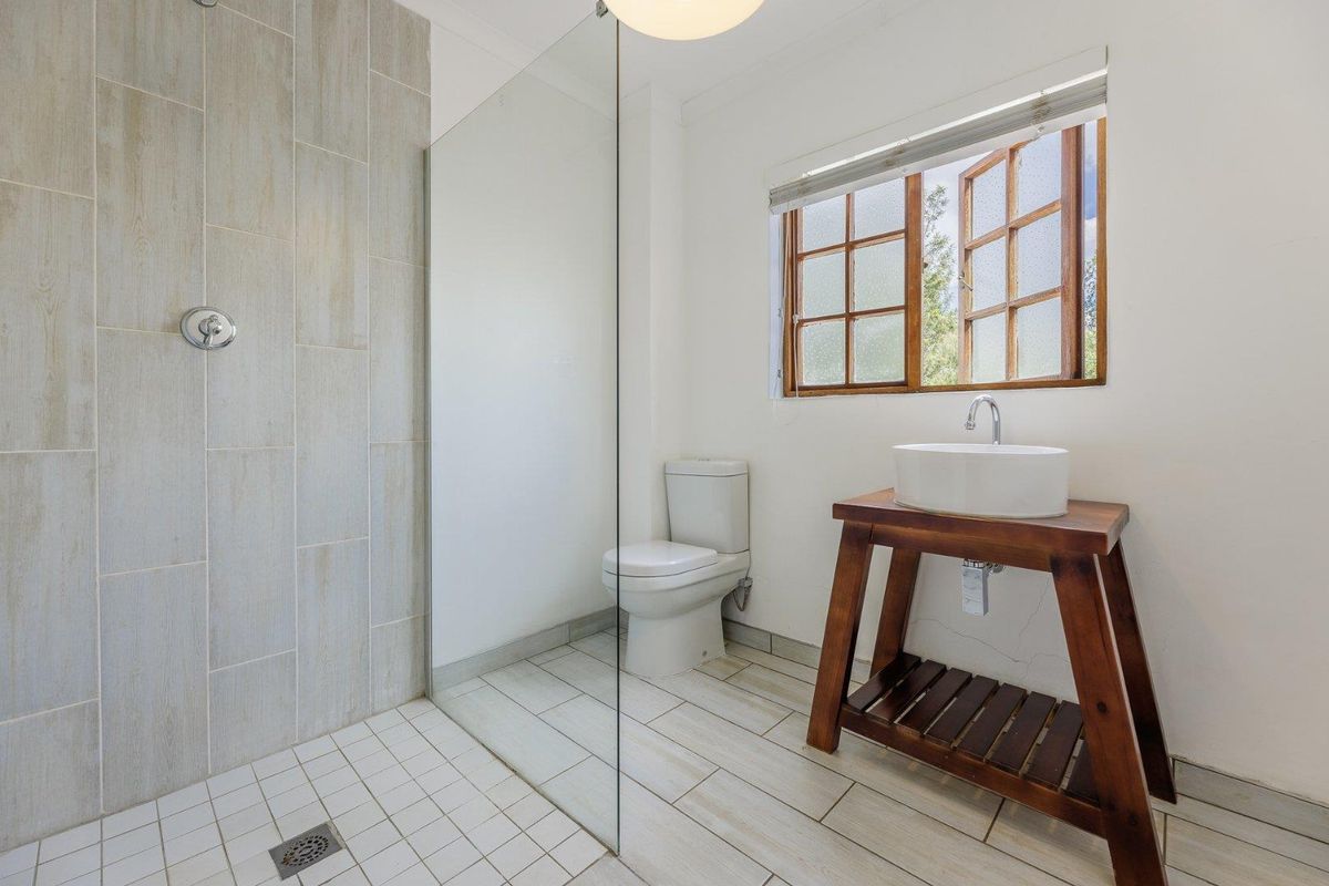 A bathroom featuring a walk-in shower with glass screen, a ceramic toilet, and a vessel sink mounted on a wooden vanity stand.