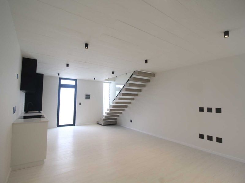 Modern open-plan living area featuring a sleek kitchen, minimalist staircase, and contemporary recessed lighting in a bright, neutral space.
