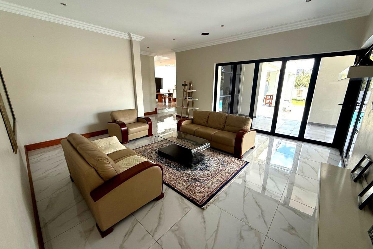 Spacious living room featuring large format marble-look floor tiles, recessed downlighting, and expansive black-framed sliding glass doors opening to the patio.