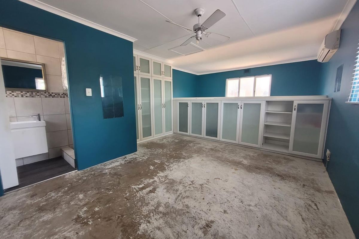 Spacious bedroom featuring built-in cabinetry, an en-suite bathroom, ceiling fan, and air conditioning. The room requires new flooring to complete the space.